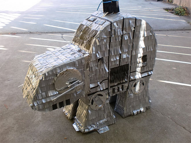 A shiny silver AT-AT pinata from Star Wars features details such as hatches and sunken areas delineated with black tissue paper. Hip joints and the side guns are made from cardboard and are covered in aluminum foil.