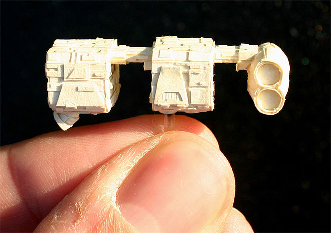 Starboard view of the Mobquet, showing its three sections connected by thin spars at the top: the rear and middle cube-shaped sections, and the bridge section at the front, which morphs from an ovular cylinder on the port side to two circular cylinders on the starboard side. Two small engines poke out from the underside of the rear section.